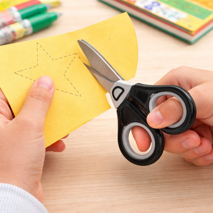 Person holding a pair of scissors over yellow paper with star cutouts on a wooden surface.