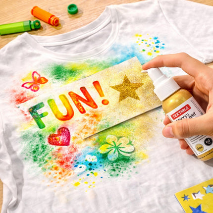 White t-shirt with colorful designs and text, being decorated with gold spray paint.