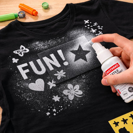 Black t-shirt with white designs being sprayed with a spray bottle on a wooden surface.