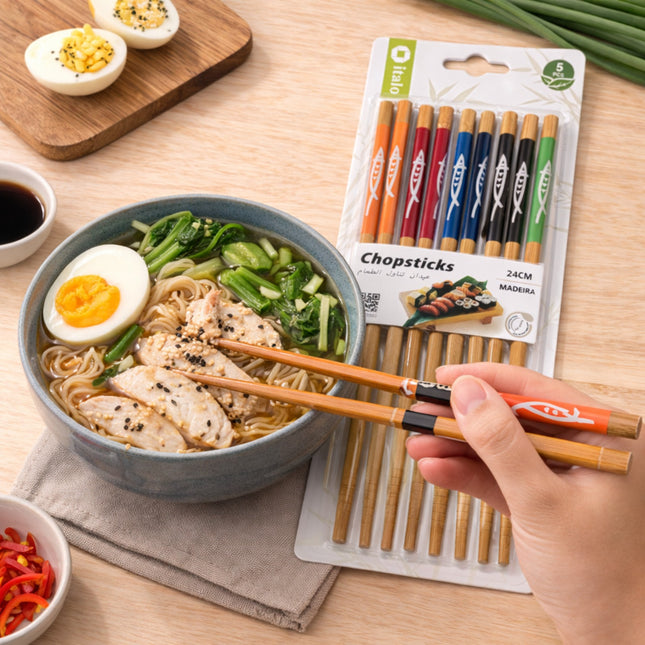 Bowl of noodles with chopsticks, a package of chopsticks, and a hand holding chopsticks on a wooden table.