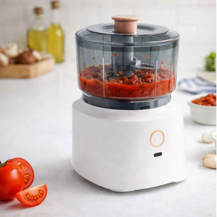 White food processor with a clear container filled with red sauce on a kitchen counter.