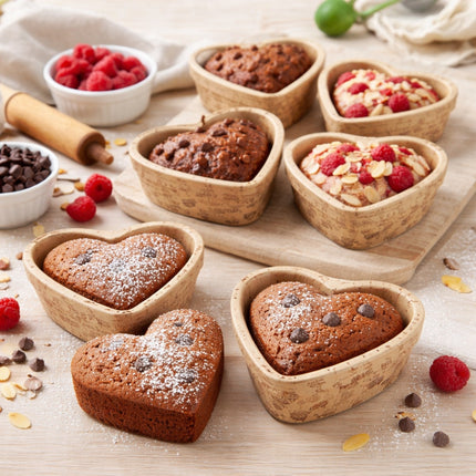 Heart-shaped cakes on a wooden surface with raspberries and baking ingredients.