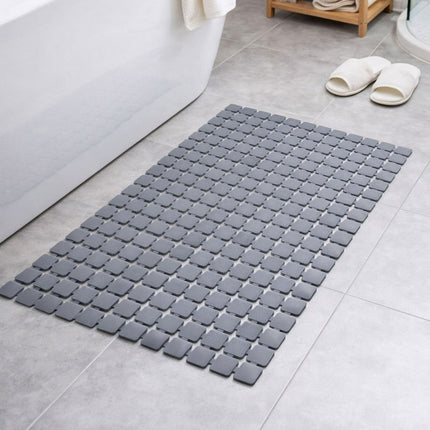 Gray bath mat on a bathroom floor with white bathtub and slippers in the background