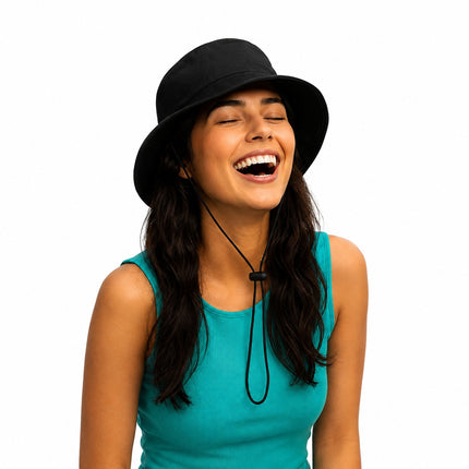 A woman wearing a black bucket hat with a chin cord and a teal sleeveless top, laughing against a solid white background.
