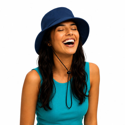 A woman with dark hair wearing a navy blue bucket hat and a turquoise sleeveless top, laughing against a solid white background.