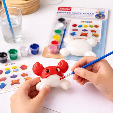 Person painting a red and white toy with a brush, surrounded by art supplies on a table.