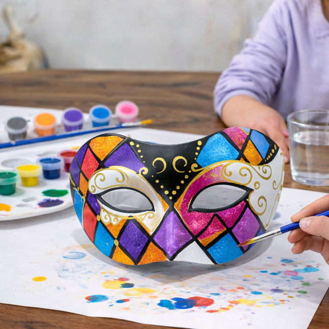 Colorful mask being painted with a brush on a table with art supplies.