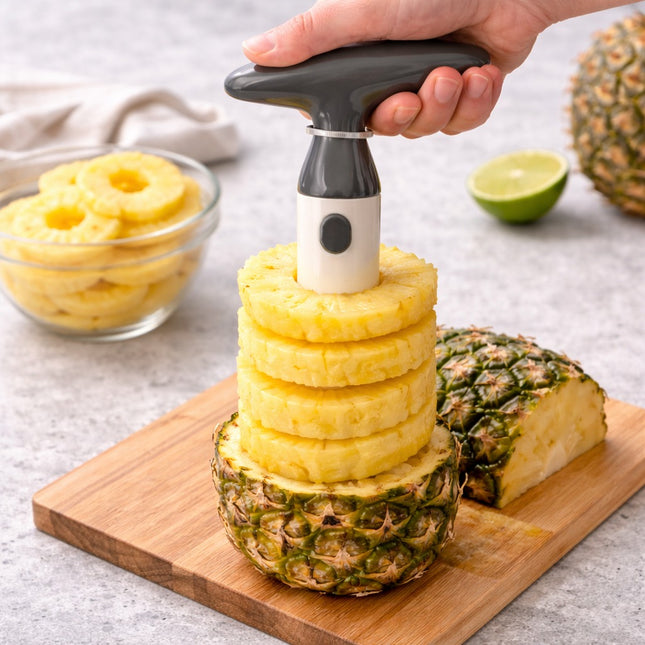Pineapple being sliced with a manual slicer on a wooden cutting board.