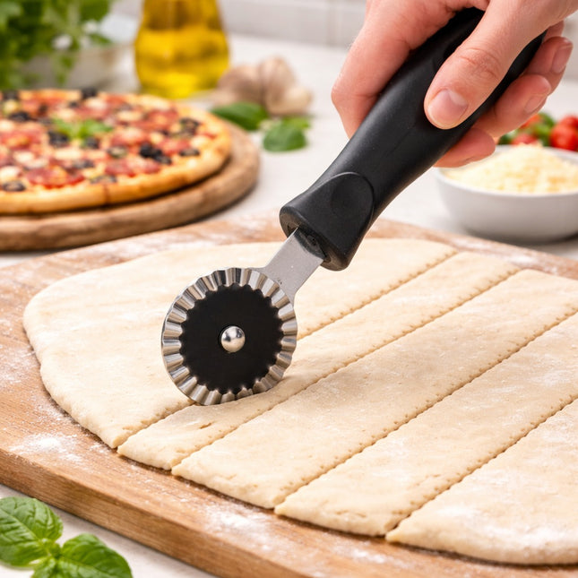 Pizza cutter being used on pizza dough with a pizza and ingredients in the background