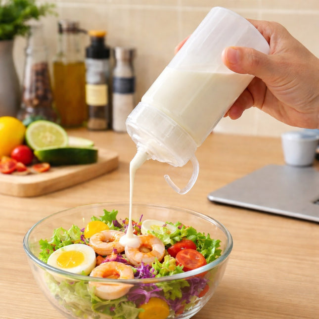 Person pouring dressing from a small container onto a salad on a wooden table.