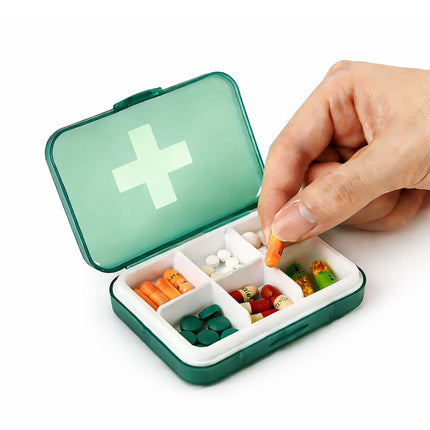 Hand placing a pill into a small green pill organizer with a white cross on a white background