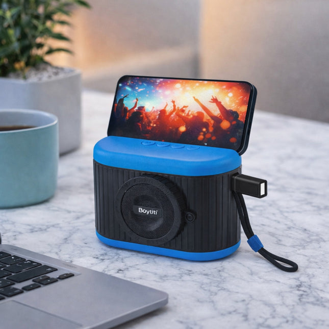 Portable speaker with smartphone dock on a marble surface, next to a laptop and coffee cup.