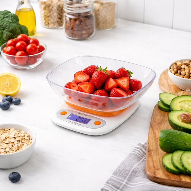 Digital kitchen scale with a bowl of strawberries on a white countertop with various fruits and vegetables.