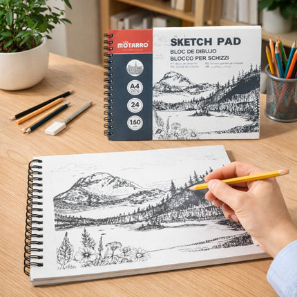 Motronro sketch pad with mountain landscape drawing on a wooden table with stationery items.