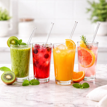 Four colorful drinks in glasses with straws on a marble surface, garnished with fruits and herbs.