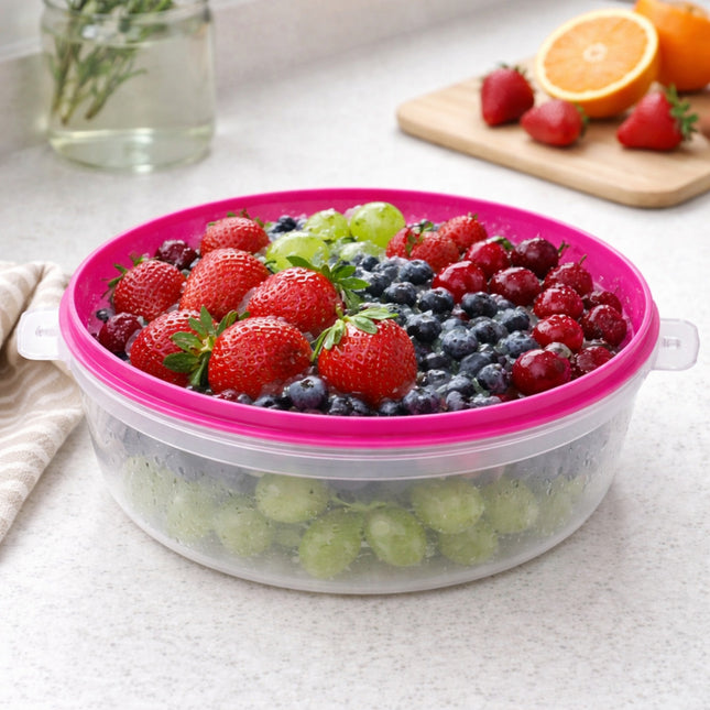 Fruit salad in a clear container with pink lid on a light surface, with strawberries, blueberries, and grapes.