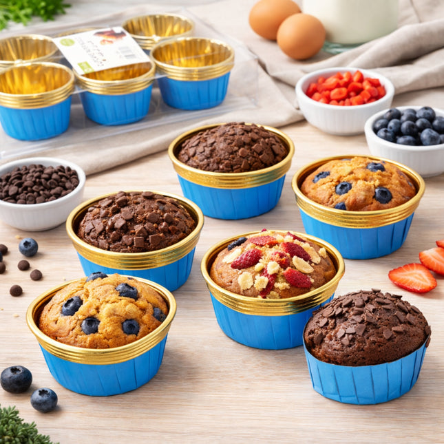 Muffins in blue and gold silicone muffin cups on a wooden surface with ingredients in the background.