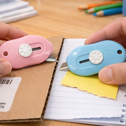 Two colorful paper cutters held by hands with a notebook and pencils in the background.