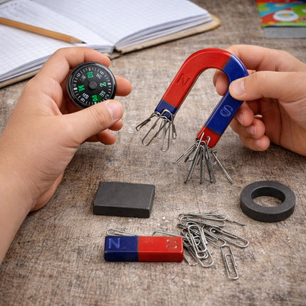 Hands holding a compass and magnetic tool with various magnetic items on a textured surface