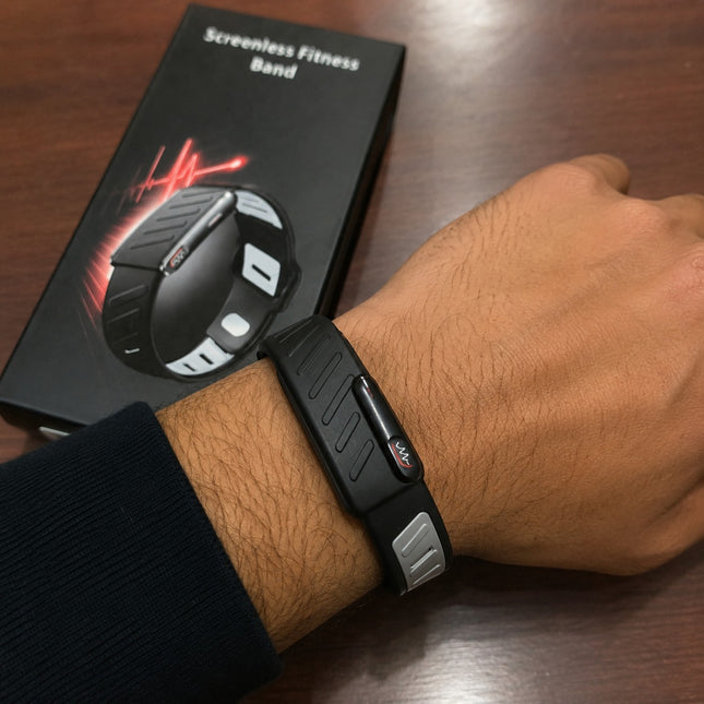 A black screenless fitness band with a silver side accent is worn on a person's wrist, with its black retail box visible in the background on a wooden table.