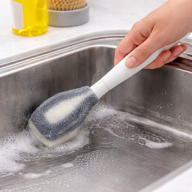 Hand using a scrubbing brush to clean a sink with soap suds.