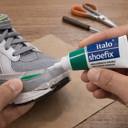 Person applying italo shoefix adhesive to a gray sneaker on a wooden surface.