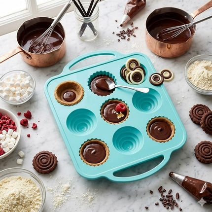 Blue silicone mold with chocolate treats on a marble surface with baking ingredients.