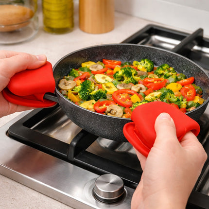 Person holding a frying pan with vegetables on a stove using red silicone handles.