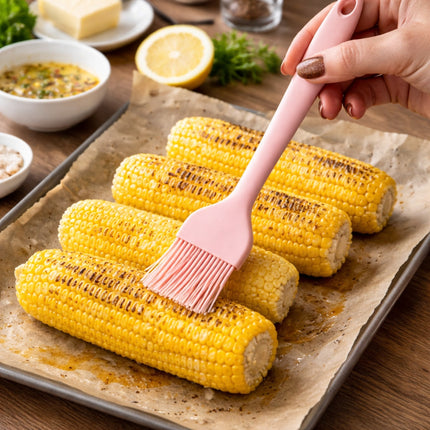 Person brushing roasted corn with a pink brush on a baking sheet.
