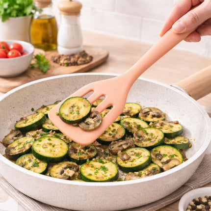 Person using a spatula to serve zucchini and mushroom dish from a white pan on a wooden table.