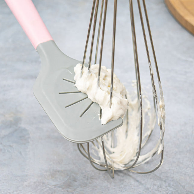 Gray spatula lifting whipped cream from a whisk on a light gray background