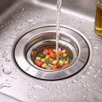 Vegetables being washed in a kitchen sink drain with water flowing over them.