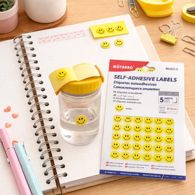 Smiley face labels on a notebook with stationery items on a desk