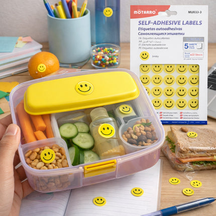 Bento box with smiley face labels on a desk with a package of smiley face labels in the background.