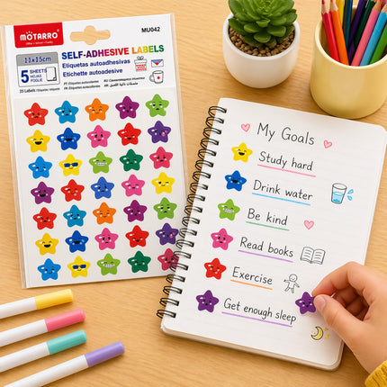 Colorful star-shaped self-adhesive labels on a sheet next to a notebook with goals and a hand placing a label on the page.