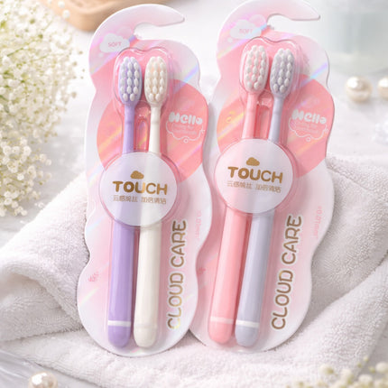 Two sets of children's toothbrushes in pink and purple packaging on a white towel with flowers in the background.