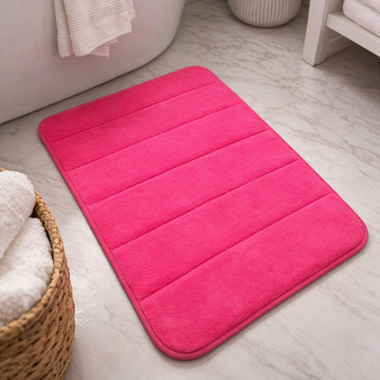 Pink bath mat on a bathroom floor with a basket of towels and a towel rack in the background.