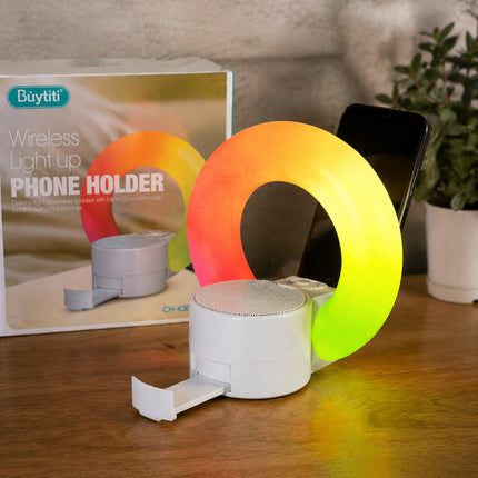 Wireless light-up phone holder with colorful design on a wooden surface, next to its packaging.