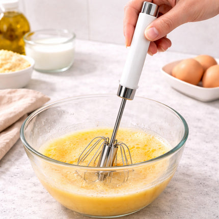 Hand using a hand mixer to blend eggs in a glass bowl on a kitchen counter.