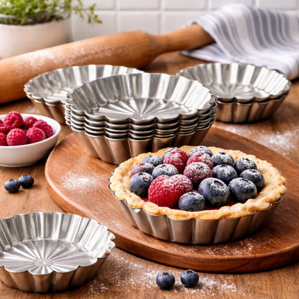Metal tart tins on a wooden surface with a berry tart and fresh berries.