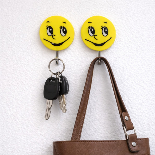 Two yellow smiley face hooks on a textured white wall with keys and a brown bag hanging from them.