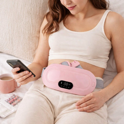 Woman using a pink waist massager while holding a phone on a bed.