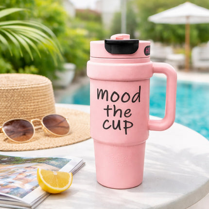 Pink travel mug with 'mood the cup' text on a table by a poolside.
