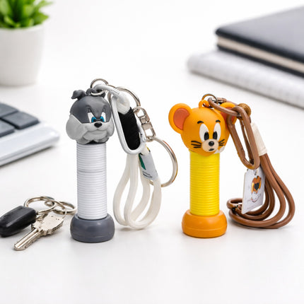 Two cartoon-themed keychains on a desk with a keyboard and plant in the background.