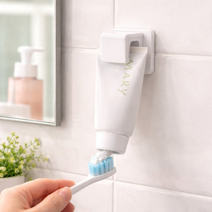 Hand holding a toothbrush with a toothpaste dispenser attached to a bathroom wall.