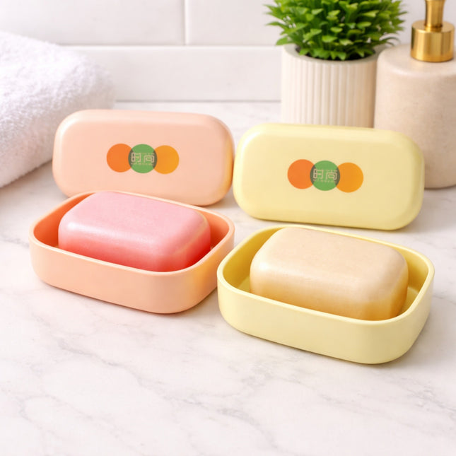 Two soap dishes with pink and beige soaps on a white surface with a plant in the background.
