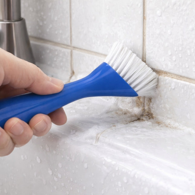 Hand using a blue scrub brush to clean a tiled wall.