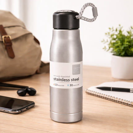 Stainless steel water bottle on a desk with a backpack, phone, and notebook in the background