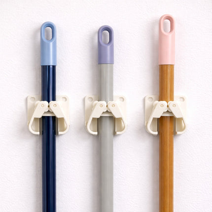 Three brooms with colorful handles attached to a white wall using holders.