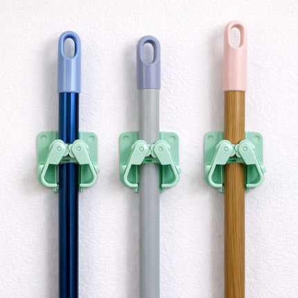 Three brooms with green holders against a white wall